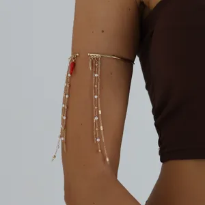 Gold upper arm cuff detail shot featuring delicate dangling tassels and red chili charm.