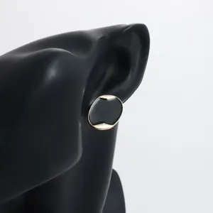 Primo piano dettagliato di orecchini a lobo geometrici neri e oro su un espositore.