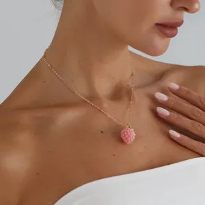 Close-up detail of dainty gold chain necklace featuring a cute pink raspberry pendant.