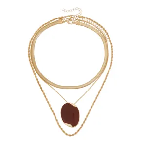 Collana dorata multistrato con catena a spina di pesce, catena cordata e ciondolo ovale rosso scuro.