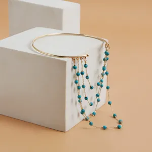 Close-up detail of a gold-tone open arm cuff featuring hanging chains with turquoise beads.
