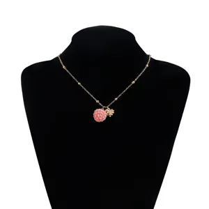 Closeup detail of cute pink raspberry pendant necklace with gold chain and flower accessory.