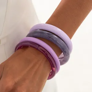 Close-up of stylish stacked purple resin bangles on wrist, smooth curved glossy finish details.