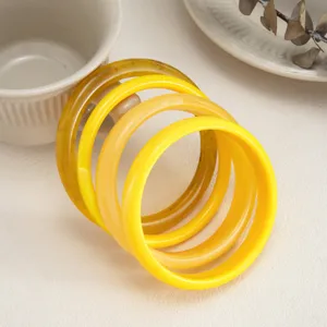 Close-up details of colorful resin bangles, smooth glossy yellow stacked bracelets set.