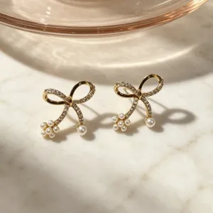Gold bow earrings with sparkling micro-set zirconia and delicate white pearl details for elegant style.