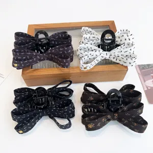 Vue détail pinces à cheveux nœud floral en tissu avec griffe plastique noire pour coiffure élégante.