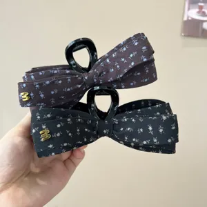 Gros plan détaillé de la pince à cheveux nœud en tissu multicouche avec motif floral et métal.