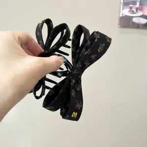 Vue détaillée d'une pince à cheveux noire à motif floral avec nœud en tissu superposé chic.