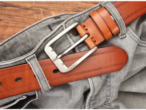 Vue détaillée d'une ceinture en cuir marron pour homme avec boucle en métal sur un jean.