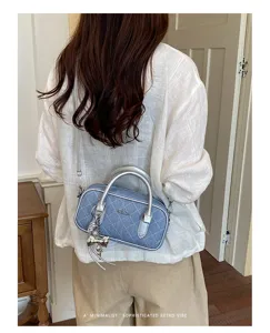 Detailed shot of a stylish blue denim quilted crossbody barrel bag with silver hardware.