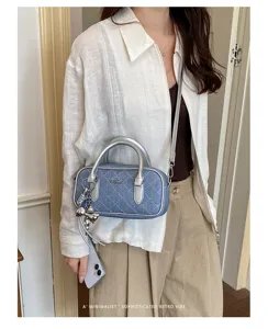 Blue denim quilted barrel handbag with silver handle and crossbody strap for women.