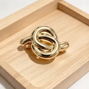Primo piano del fermaglio per capelli a nodo in metallo dorato su vassoio di legno.