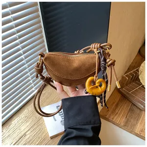 Brown suede half-moon dumpling bag detail showing delicate knotted straps and cute charm.