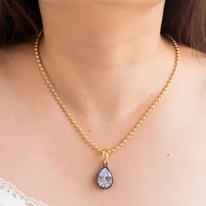 Detalle en primer plano de un collar de cadena dorada con colgante de circonita en pera.