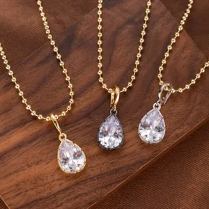 Primer plano detallado de tres collares con colgante de circonita en gota en madera.