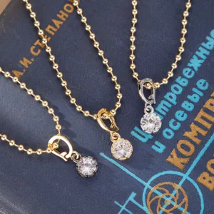 Detalle de tres collares de cadena de bolas con colgantes de circonita redonda en negro, oro y plata.
