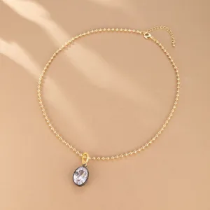Primer plano de un collar de cadena de cuentas doradas con un colgante de circonita.