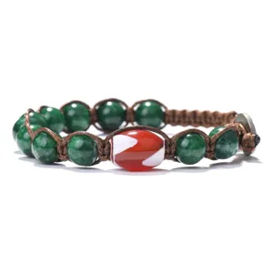 Close-up detail of handmade woven bracelet with green beads and central red dzi bead.