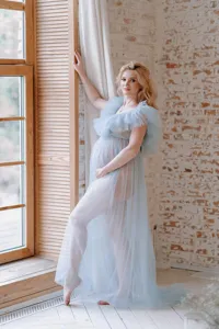 Détail de la robe de maternité en tulle doux, tissu bleu clair transparent, scène élégante.