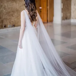 Elegant white wedding dress with long sheer cape for bridal photography and studio shoots.