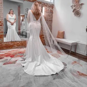 Elegant white wedding dress featuring a long sheer cape and sweeping train for brides.