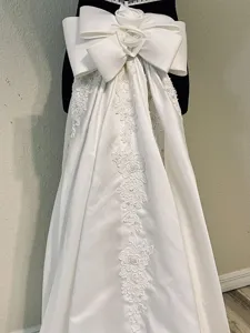 White satin wedding skirt detail showcasing large bow and intricate lace embroidery train.