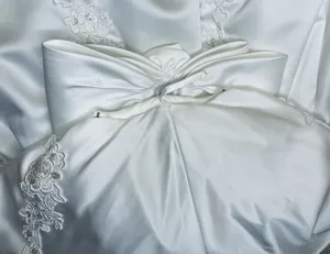 White satin wedding dress detail close up showing elegant bow and beaded lace appliques for bride