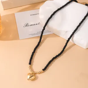 Primer plano detalle del collar de cuentas negras con colgante de corazón dorado en expositor.