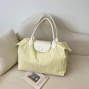 Vue détaillée d'un sac cabas plissé jaune clair élégant avec des poignées blanches.