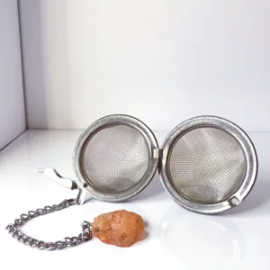 Stainless steel tea strainer detail showing mesh sphere, chain, and crystal stone pendant inside.