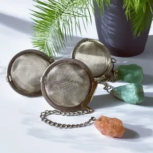 Stainless steel tea infuser detail showing mesh basket, chain, and raw crystal pendant.