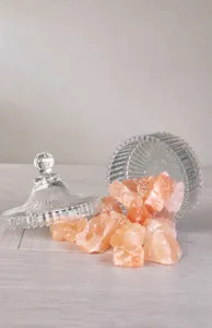 Primer plano detallado de rocas de sal rosa natural presentadas en un frasco de vidrio.