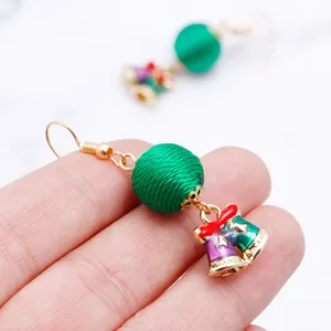 Close-up detail of Christmas themed bell earrings featuring green thread balls and enamel bells.