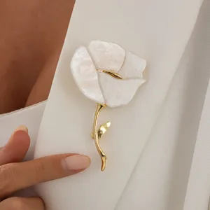 Elegant white flower brooch with gold stem, detailed close-up shot worn on white jacket lapel.