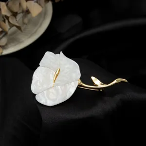 Exquisite close-up of a white flower brooch with gold stem on black satin background.