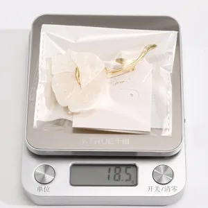 Close-up detail of white acrylic flower brooch with gold metal stem, elegant fashion jewelry piece.