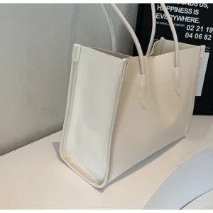 Detail view of a minimalist beige soft leather tote bag, showing fine texture and dual straps.