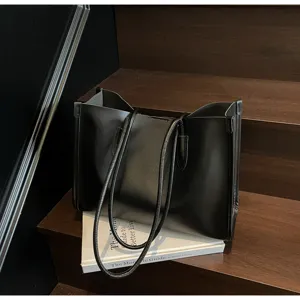Close-up detail of a black soft leather shoulder tote bag placed on wooden steps.