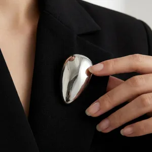 Detail van zilveren druppelvormige broche op klassieke zwarte blazer, elegant mode-accessoire.