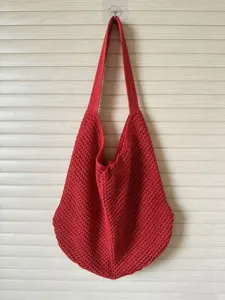 Detailed view of the red crochet shoulder bag showing the hollow knit pattern and texture.