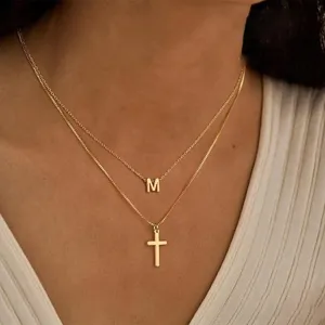 Collier double couche doré avec pendentif lettre M et croix détail au style élégant.