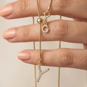 Détail de collier initiale Y en or avec breloques de lettres en zircon et perle ajustable.