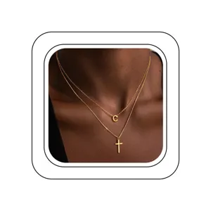 Gros plan sur un collier doré double couche avec un pendentif lettre C et une croix.
