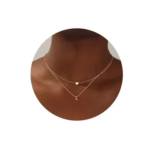 Primer plano detallado del collar dorado de doble capa minimalista con colgante y letra L.