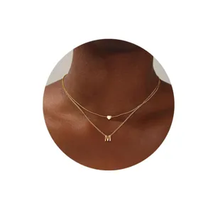 Primer plano detallado de un collar dorado doble minimalista con dijes de corazón y letra M.