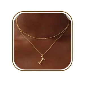 Detailopname van de dubbele gouden ketting met delicate kralenkettingen en stijlvolle letterhanger.