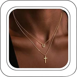 Gros plan de colliers dorés à double superposition avec pendentif lettre U et croix au cou.