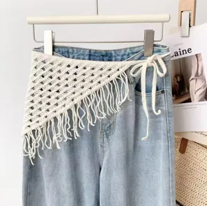Detailed view of white crochet fringe triangular waist scarf accessory tied on blue jeans.