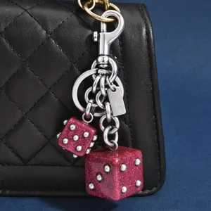 Détail de bijou de sac double dé avec des dés roses pailletés et du métal argenté.