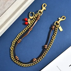 Trendy gold chain bag strap with cute red cherry charm and brown leather weave details.